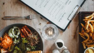 Top view of wooden table with served healthy veggie salad and french fries placed near menu and spices
