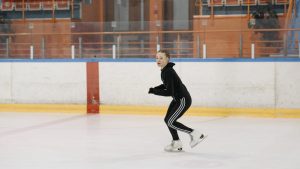 A young girl practicing figure skating in an indoor ice rink, wearing a black outfit.